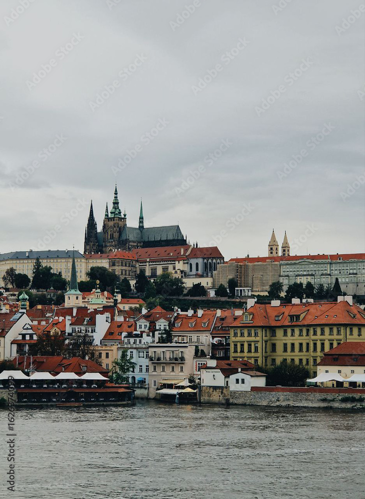 Obraz premium Beautiful view of Prague Castle and riverside buildings under a gray sky during early evening