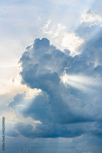 Dramatic cumulus clouds illuminated by sunlight. Bright rays of sunshine pierce through the cloudscape, creating a serene and majestic sky scene.