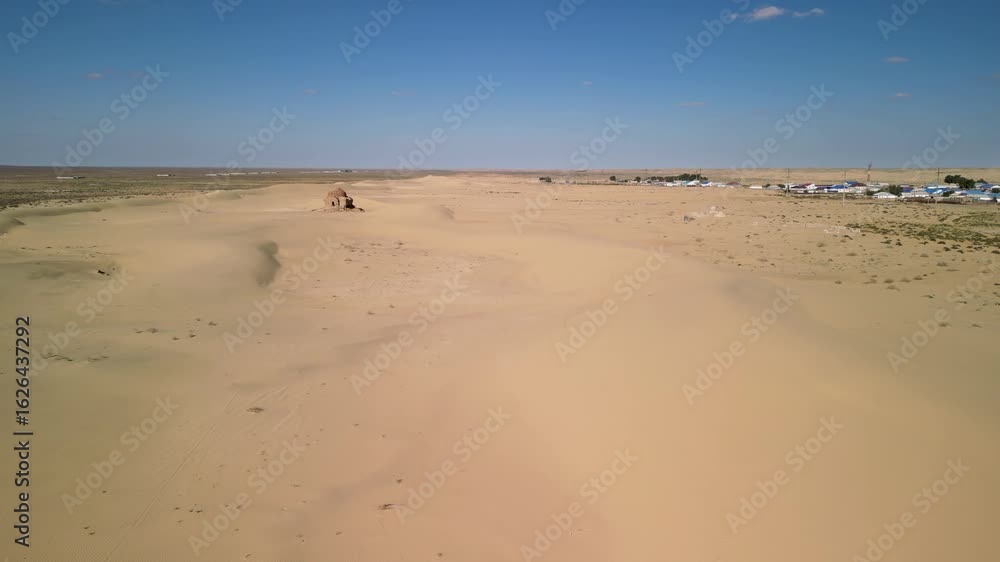Aerial view of dunes, small village, and ancient tomb among golden sands. Aral Sea region, Kazakhstan. Aerial view of dunes, small village, and ancient tomb among golden sands. Aral Sea region, Kazakhstan.
