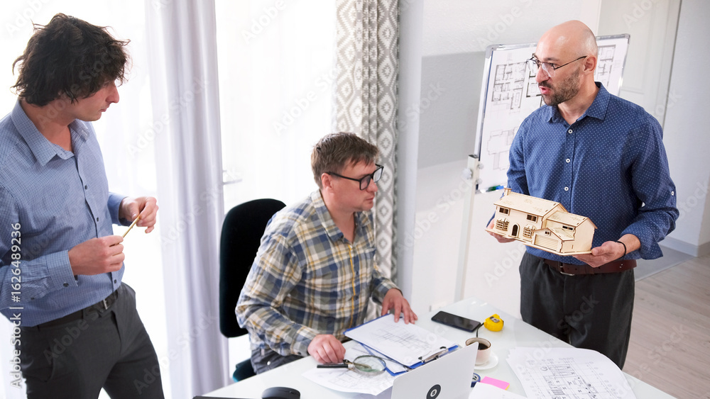 Obraz premium A team of engineers is designing a smart home model. Three men are discussing the design of the building. One of the men holds a model in his hands