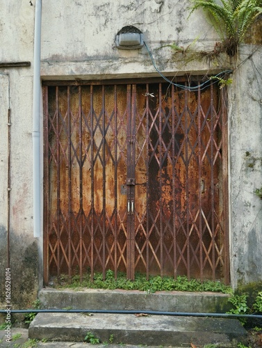 An old, rusty metal grille sliding door, often referred to as a collapsible door grille or a security grille, which serves as a protective barrier for entrances. 