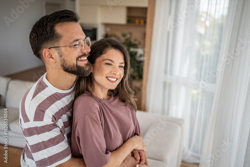 Free Download Happy couple embracing and smiling in modern apartment - GFXLoad