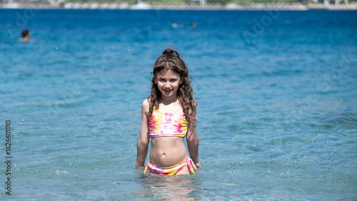 A sweet little girl child joyfully playing in the sea during vacation, enjoying the summer