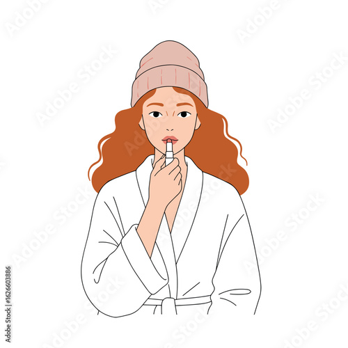 Young woman in robe applying lipstick while looking at camera  