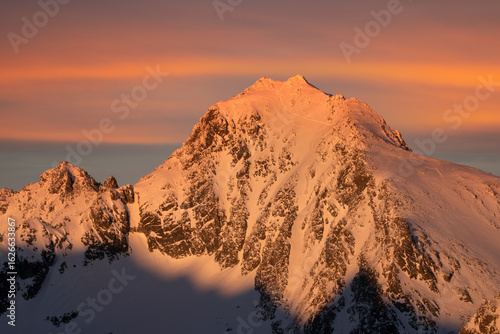Aerial view of a majestic, snow-dusted peak bathed in the warm glow of the setting sun, casting long shadows across its craggy face, VysokÃ© Tatry, PreÅ¡ov Region, Slovakia.