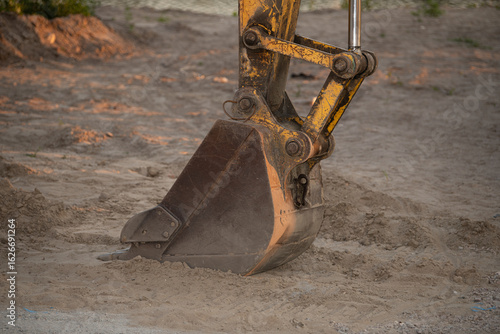 A large excavator is engaged in digging at a construction site in the late afternoon. The sandy soil is disturbed as the machine operates efficiently