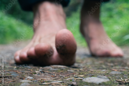 A closeup of bare feet walking on a forest trail with soil and stones
