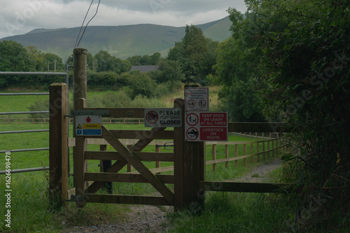 A wooden gate on a rural path with warning signs about keeping the gate closed and dogs on a leash in a picturesque landscape