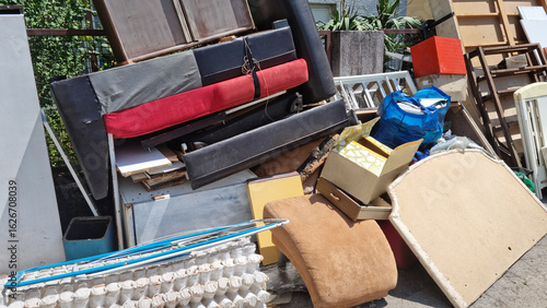 A large, disorganized pile of discarded household items, including parts of furniture, old sofas, and miscellaneous junk, piled up outdoors for bulky waste collection