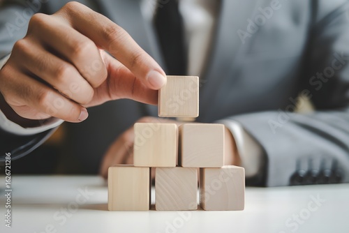 Building a Firm Foundation: A businessperson strategically places wooden blocks, symbolizing the critical construction of a solid groundwork for future expansion and success.