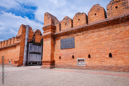 tha phae gate in chiang mai, thailand, a historic brick wall and wooden gate under a partly cloudy sky, showcasing ancient architecture of the old city moat and entrance
