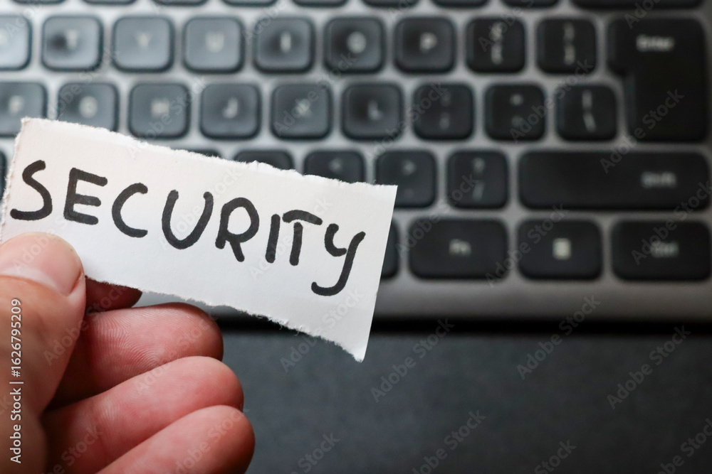 Naklejka premium A person holding a torn piece of paper with the word SECURITY against a blurred computer keyboard background, symbolizing cybersecurity awareness and protection.