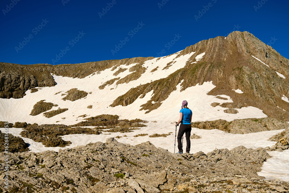 Obraz premium Rear view of a woman with trekking poles resting while climbing a mountain.