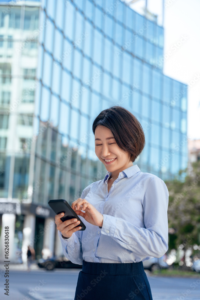 Asian mature business woman manager using cell phone mobile. Smiling female businesswoman standing outside holding smartphone for trading, banking online on city background. Vertical, copy space Asian mature business woman manager using cell phone mobile. Smiling female businesswoman standing outside holding smartphone for trading, banking online on city background. Vertical, copy space