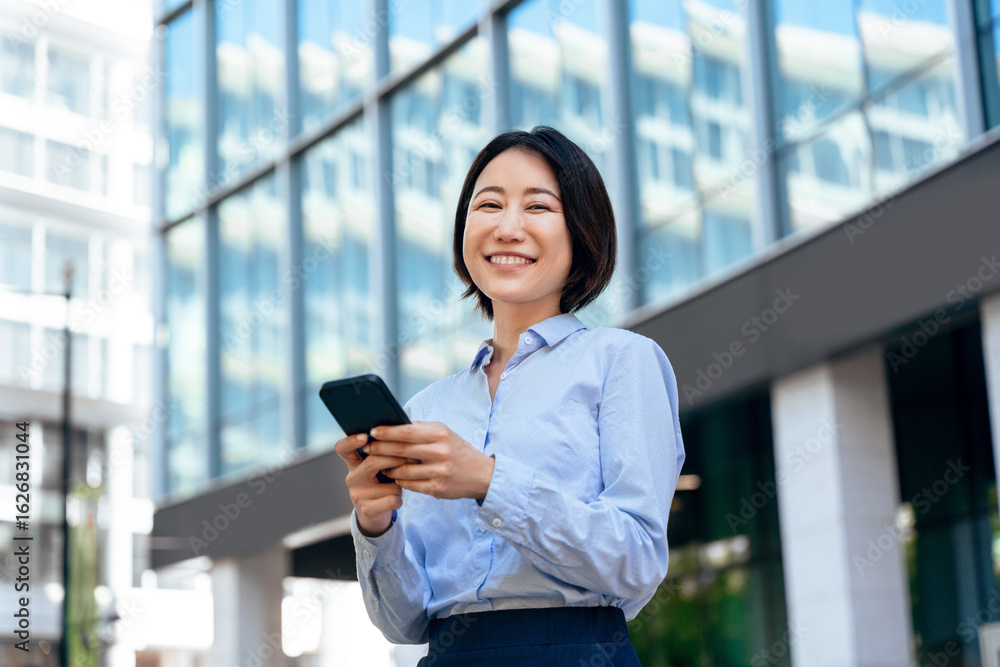 Smiling mature female businesswoman holding smartphone at office for transaction, work online looking at camera. Young Asian business woman manager ceo using cell phone mobile app outdoors. Copy space Smiling mature female businesswoman holding smartphone at office for transaction, work online looking at camera. Young Asian business woman manager ceo using cell phone mobile app outdoors. Copy space