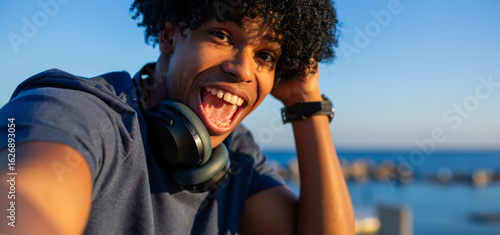 Quadro su tela Excited young mixed race man taking a wide-open smile selfie at the beach