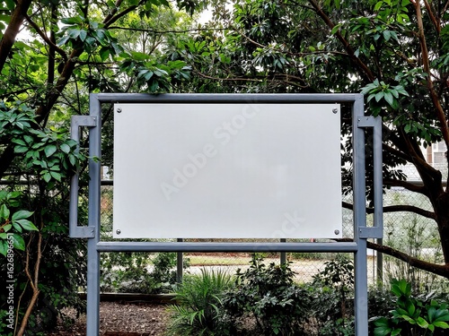 Empty white billboard surrounded by greenery in a park setting with room for text