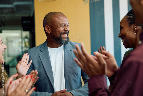 Group of diverse coworkers applauding mature businessman in office during daytime