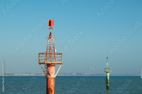 Red and green maritime lateral navigation beacons marking coastal channel in sea