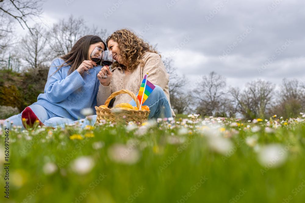 Fototapeta premium Lesbian couple enjoying wine at a romantic picnic in a blooming meadow