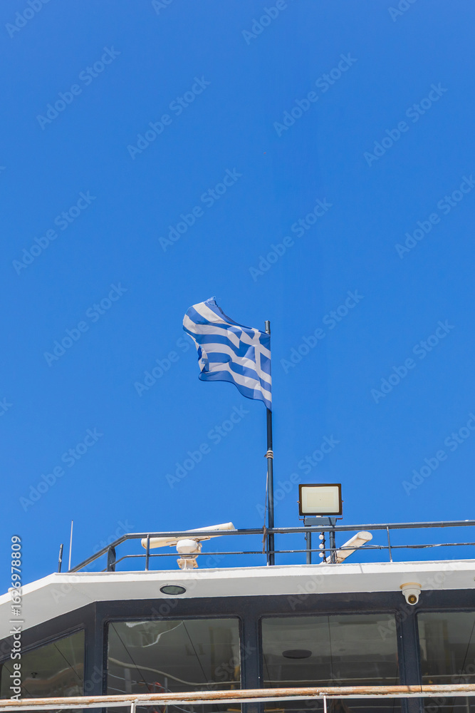 Traditional Greek blue and white striped flag waving on ferry deck, under perfect Mediterranean blue sky during summer voyage. Traditional Greek blue and white striped flag waving on ferry deck, under perfect Mediterranean blue sky during summer voyage.