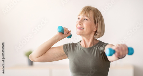Domestic sports training. Positive senior woman doing exercises with dumbbells, strengthening her body at home. Fit mature lady working on her biceps muscles, staying healthy during covid quarantine