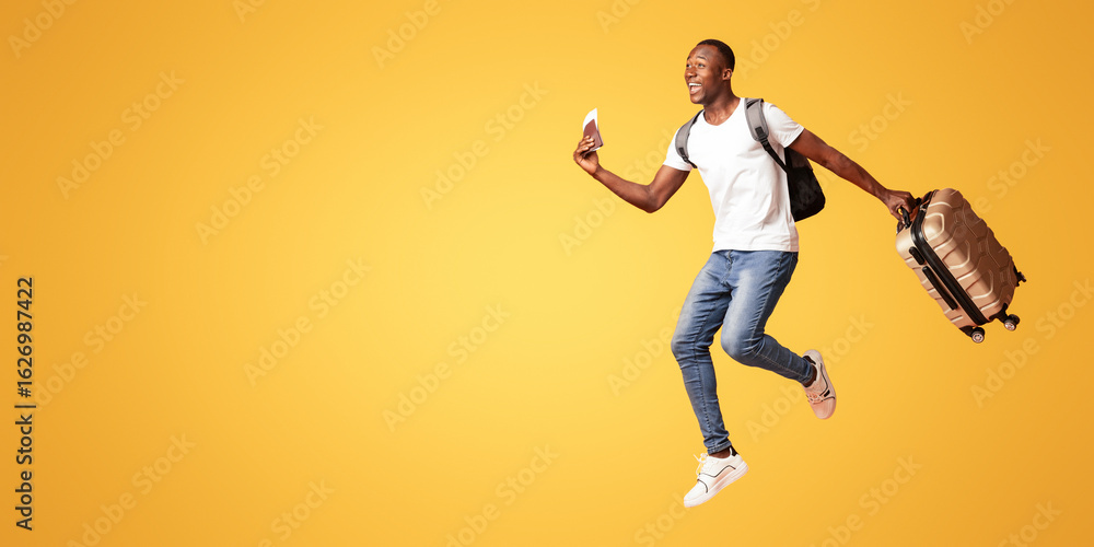 Finally vacation. Young happy black man with suitcase, backpack, passport and flight tickets jumping up orange studio background. Excited african american guy running towards copy space, panorama Finally vacation. Young happy black man with suitcase, backpack, passport and flight tickets jumping up orange studio background. Excited african american guy running towards copy space, panorama
