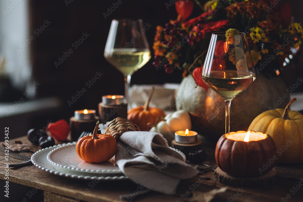 Naklejka premium Fall composition. Orange pumpkins, flowers and candles on wooden table. Family elegant Thanksgiving or halloween dinner. Cozy autumn concept, simple handmade decoration, countryside style, wine