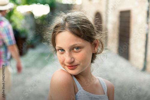 Принти на полотні A striking outdoor portrait of a young girl standing in natural light, looking directly at the camera with a calm, confident expression