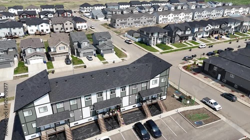 Residential area with many houses and apartments. The houses are mostly white and black. There are many cars parked in the parking lot