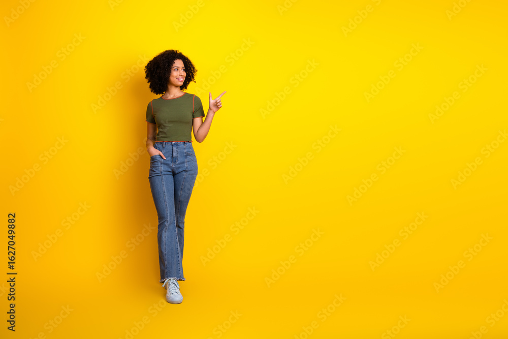 Obraz premium Confident young woman pointing towards empty yellow background, stylish in casual outfit with charming smile