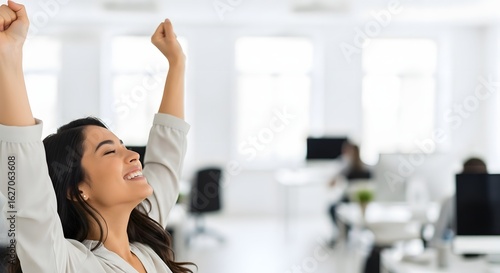 A woman in an office setting, celebrating with her arms raised in the air.