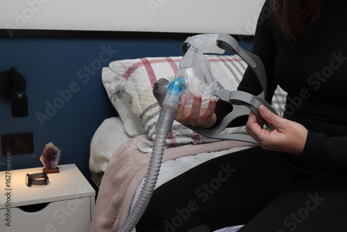 Adulto woman adjusting a cpap mask prior to sleep to treat an apnea disorder
