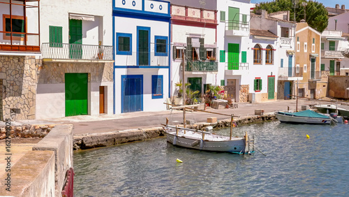 a side on view of fishing boats and colorful buildings at the marina of portocolom on mallorca, spain