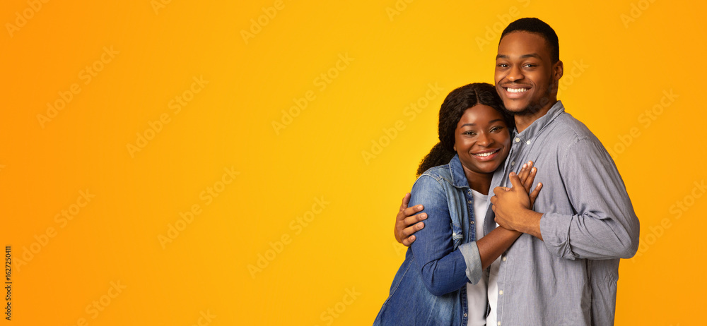 Fototapeta premium Portrait Of Affectionate Cheerful African American Couple Embracing While Posing Over Yellow Background, Happy Romantic Black Young Man And Woman Hugging And Smiling At Camera, Copy Space
