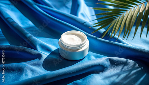 Cream Jar on Silken Fabric: A minimalist aesthetic showcases a pristine cream jar, elegantly positioned atop flowing, deep-blue fabric, with a hint of a green leaf, evoking a sense of luxury, beauty.