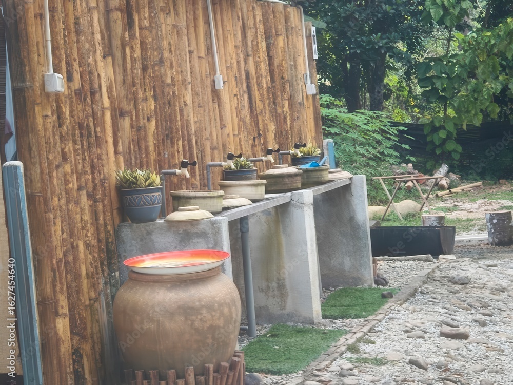 Obraz premium Outdoor water station with clay pots and bamboo backdrop in a lush garden setting