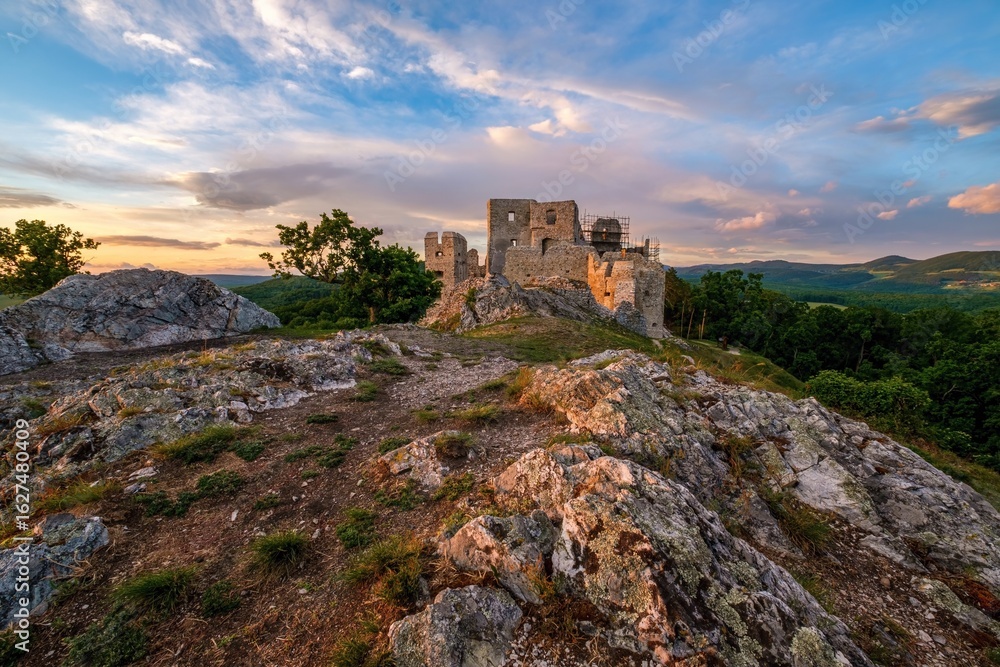Obraz premium Medieval building illuminated by the setting sun and blue sky with clouds. Ruins of Hrusov Castle, an ancient feudal castle located in West Slovakia near city Nitra. History old Hungary and Austria.
