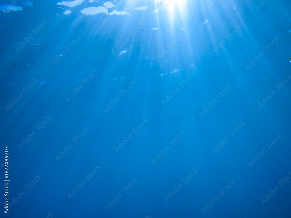 Obraz premium Dark blue ocean surface seen from underwater. Abstract waves underwater and rays of sunlight shining through, Sun light rays undersea deep, Underwater background with sea bottom, Mediterranean sea.