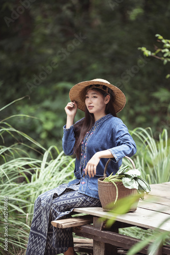 A calm and serene young woman adjusts her hat while sitting in a lush, green environment. A portrait of introspection and quiet contemplation in a peaceful, natural setting.