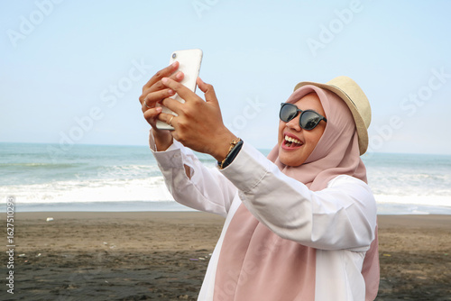 Muslim woman taking selfie on the beach in hijab