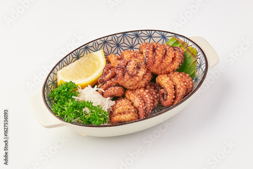 Crispy fried octopus tentacles served in decorative bowl with fresh parsley, shredded radish, lemon wedge, and green garnish, offering delightful and savory presentation