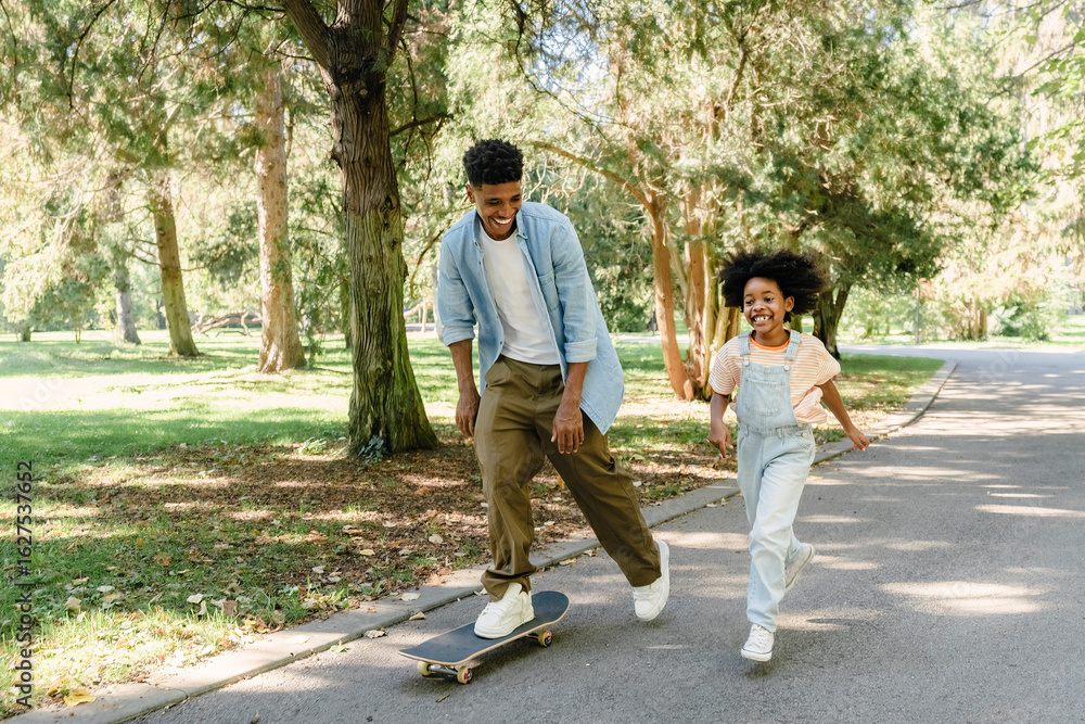 Father skateboarding with daughter in park enjoying leisure time Father skateboarding with daughter in park enjoying leisure time
