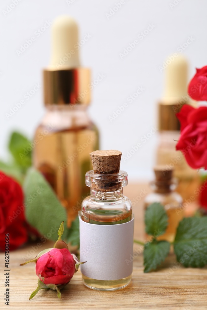 Bottles of essential oils, red roses and herbs on wooden table, closeup Bottles of essential oils, red roses and herbs on wooden table, closeup
