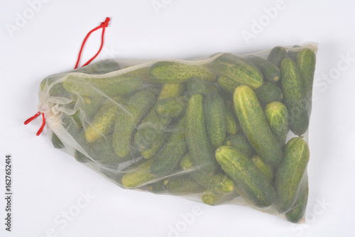 A mesh bag filled with fresh, whole pickling cucumbers is placed diagonally on a plain white background