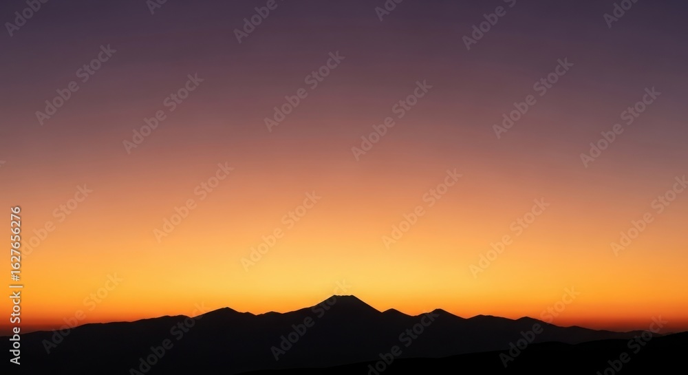 Fototapeta premium Silhouette of a conical mountain peak against a gradient sunset sky of orange purple and yellow image