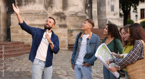 Fotografija Guide with microphone and group of tourists on city street during excursion