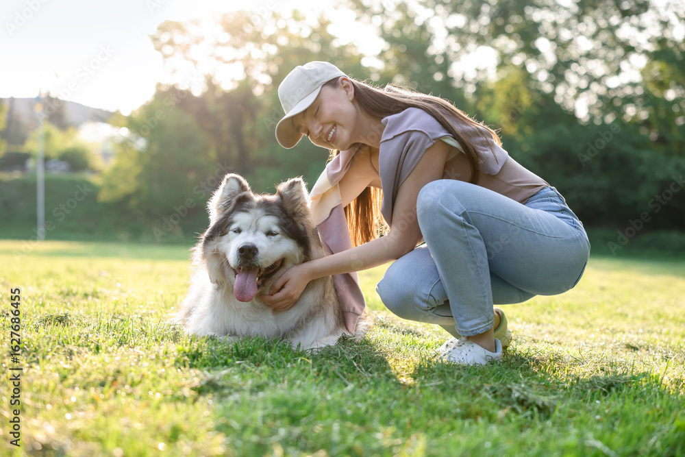Obraz premium Smiling woman with her cute Alaskan malamute dog on green grass outdoors in morning