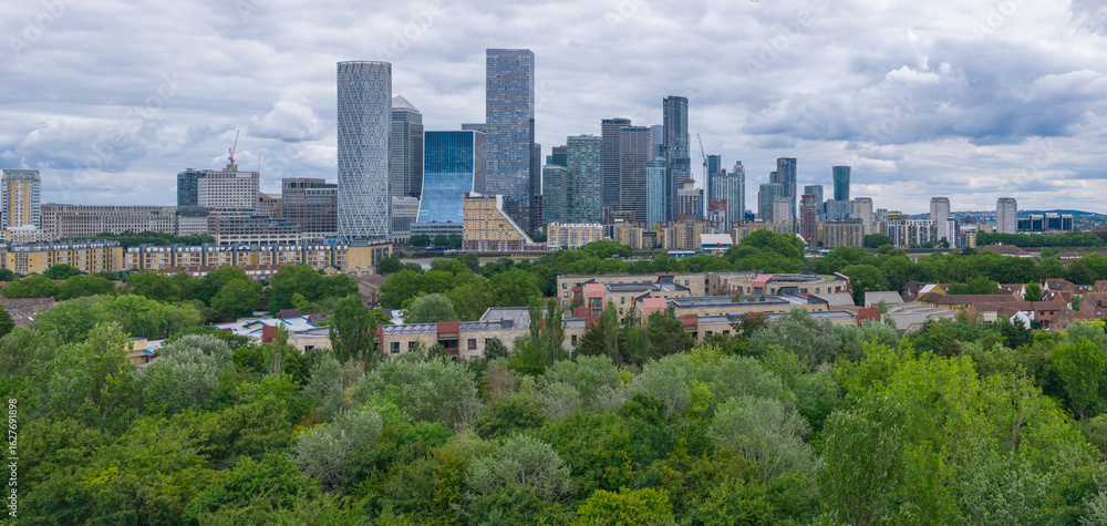 Obraz premium Canary Wharf skyline seen from the west, rising behind trees and low-rise homes.