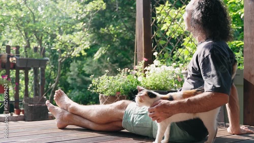 A gentle man strokes a cat while sitting on the sunny terrace of a country house